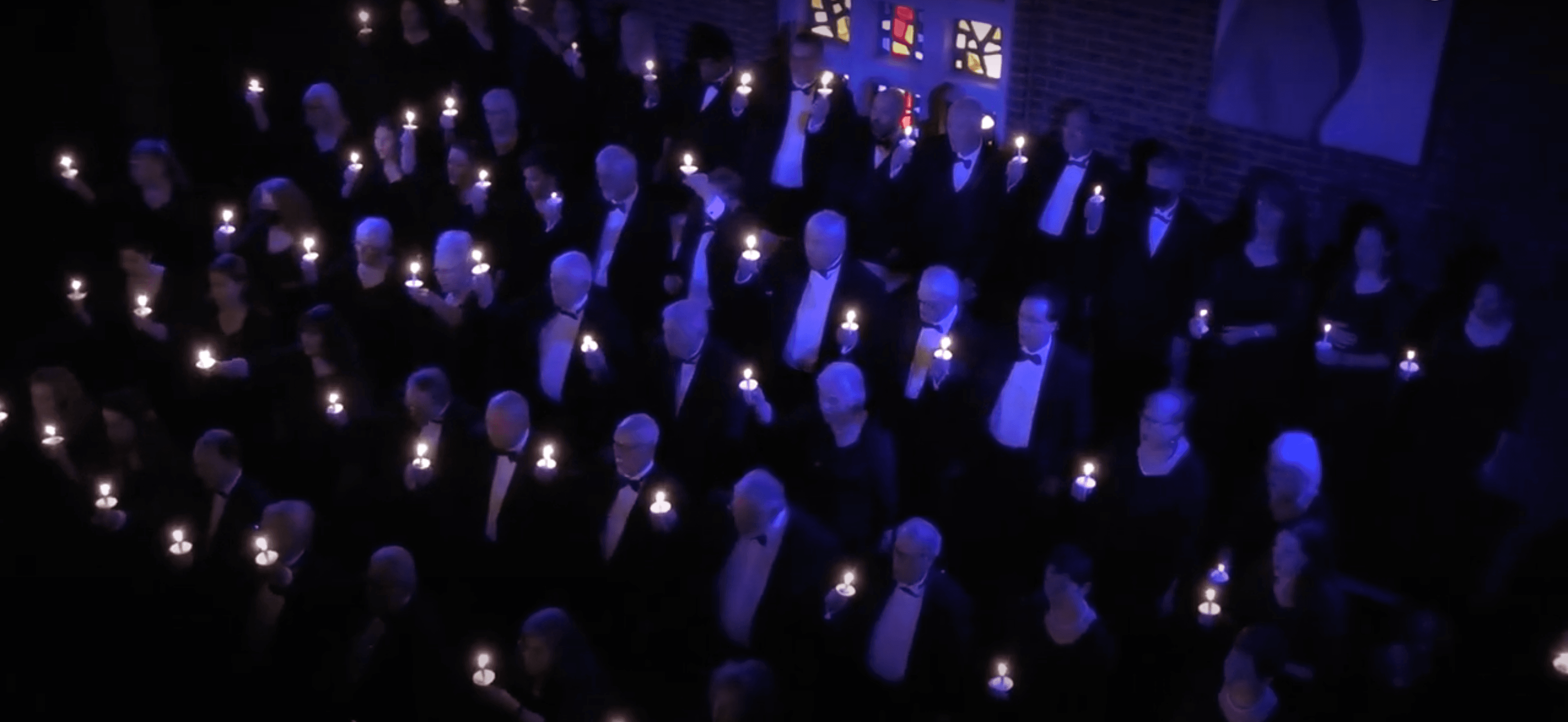 The Soli Deo Gloria Choir in black formal wear, each singer holding a lit candle in a darkened sanctuary